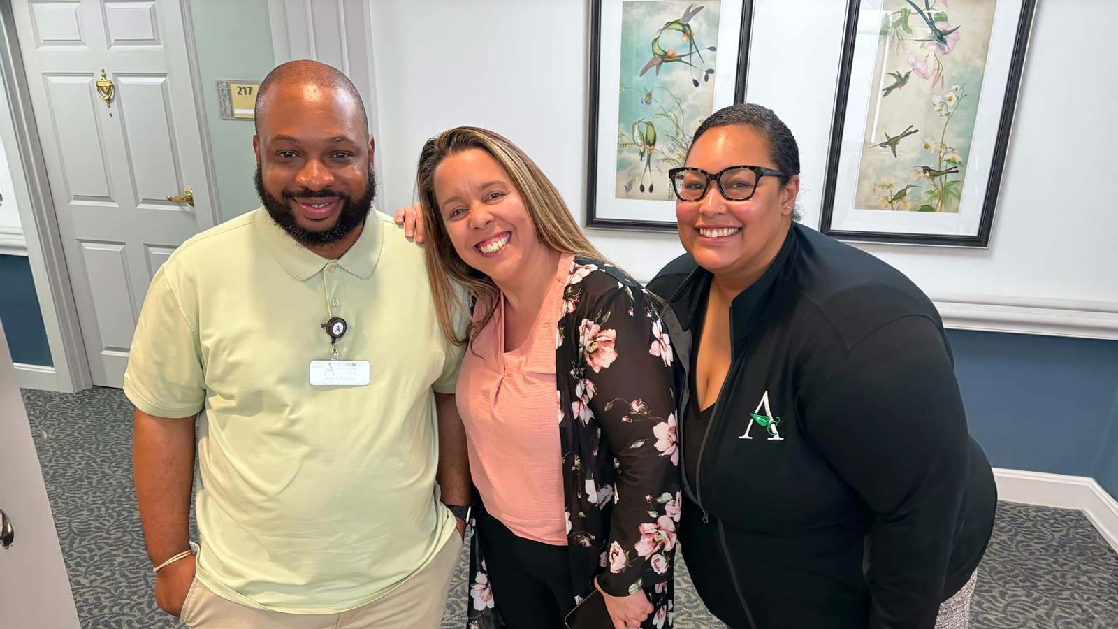 Arrow Senior Living team members smiling and posing together in a hallway, showing camaraderie and team spirit.