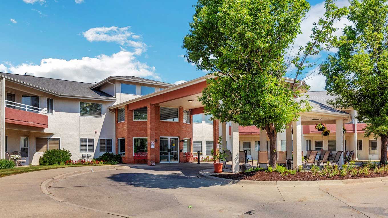 The exterior of Walden Place Senior Living community building with a welcoming entrance, large windows, and a well-maintained garden under a clear blue sky.