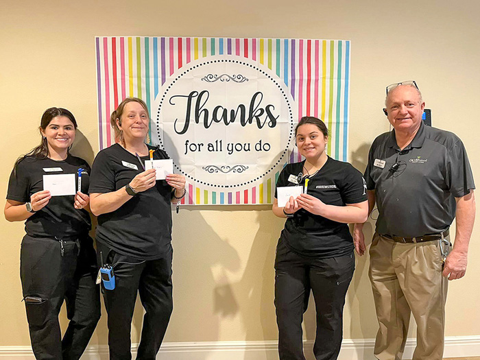 Four people holding thank you cards in front of a banner at a celebration event.