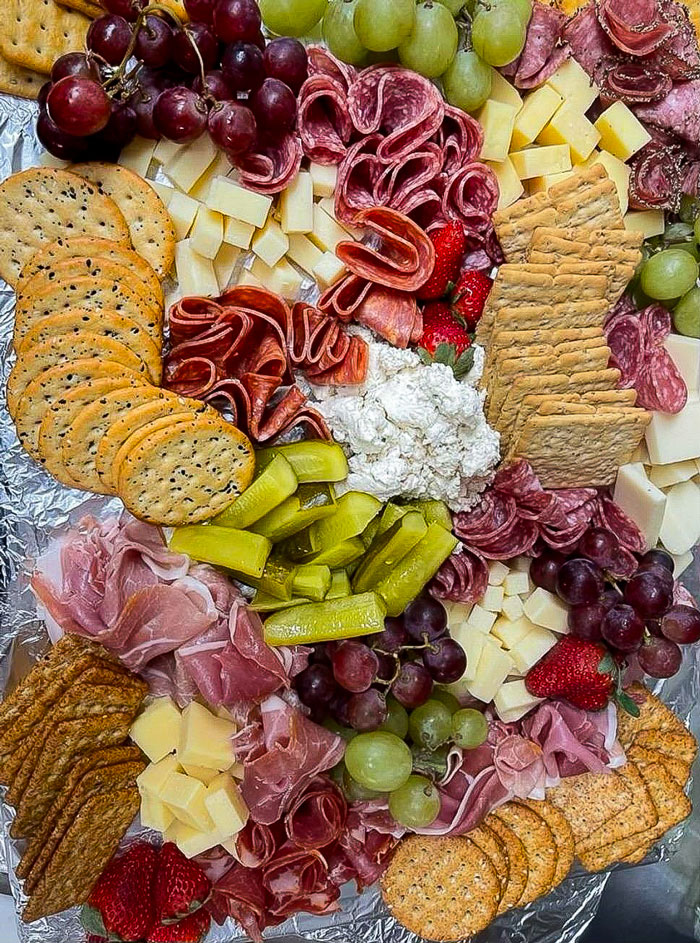 Vibrant charcuterie board featuring an assortment of sliced meats, cheeses, crackers, pickles, grapes, and strawberries, beautifully arranged for a gathering.