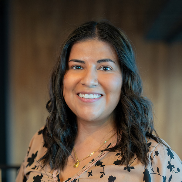 Diana Marquez, Business Operations Director at Walden Place Senior Living, smiling warmly in a floral blouse with a gold necklace, standing indoors with a soft-focus background.