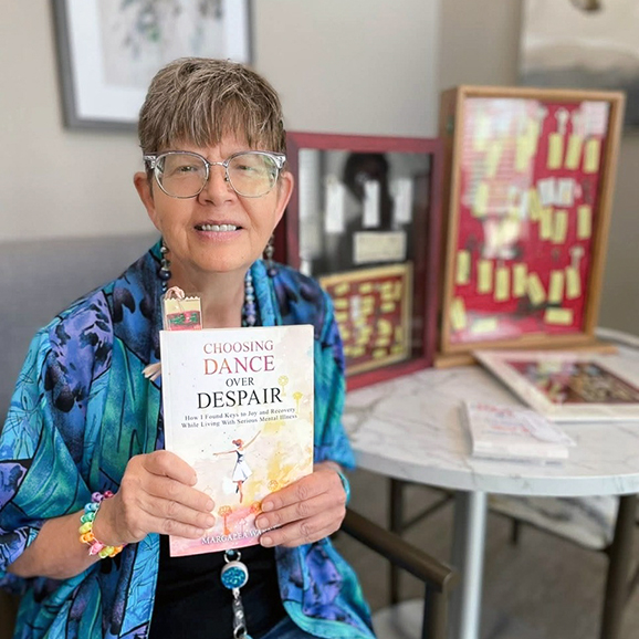 Woman smiling while holding the book "Choosing Dance Over Despair" during a senior living event.