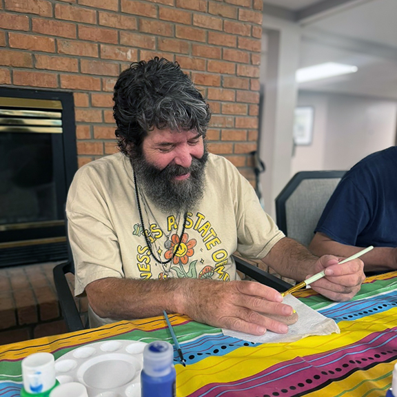 Man with a beard enjoys painting during an arts and crafts event at a senior living community, expressing creativity and relaxation in a cheerful atmosphere.