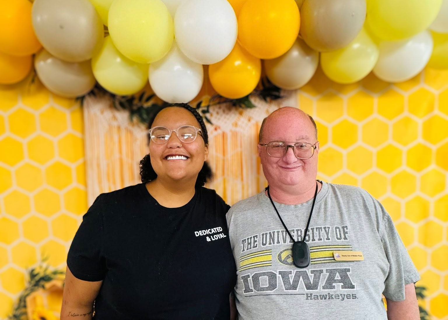 A smiling team member and resident pose together in front of a yellow backdrop and balloons.