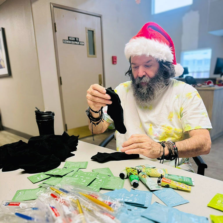 A senior man at Walden Place Senior Living works on a Christmas project while wearing a Santa hat.