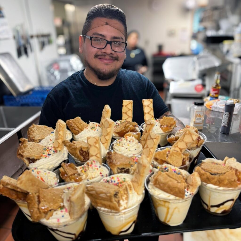 A culinary team member smiles while displaying a tray full of decadent dessert cups topped with pastries.