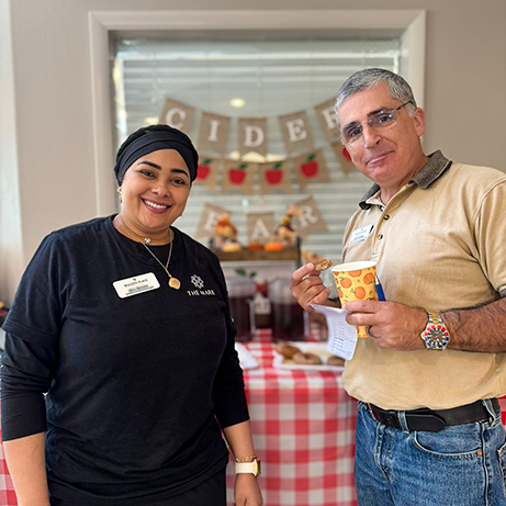 A team member smiles alongside a senior man a community gathering.