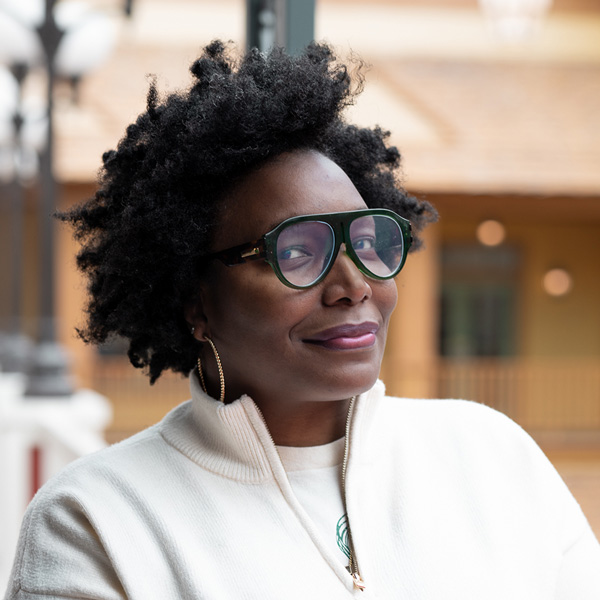 K.C. Ross, Culinary Director at Walden Place Senior Living, smiling in a professional headshot, wearing glasses and a light sweater, with a softly blurred outdoor community background.