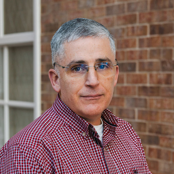Jeff Steadman, Plant Operations Director at Walden Place Senior Living, smiling in a professional headshot, wearing glasses and a red checkered button-down shirt, with a softly blurred brick and window background.