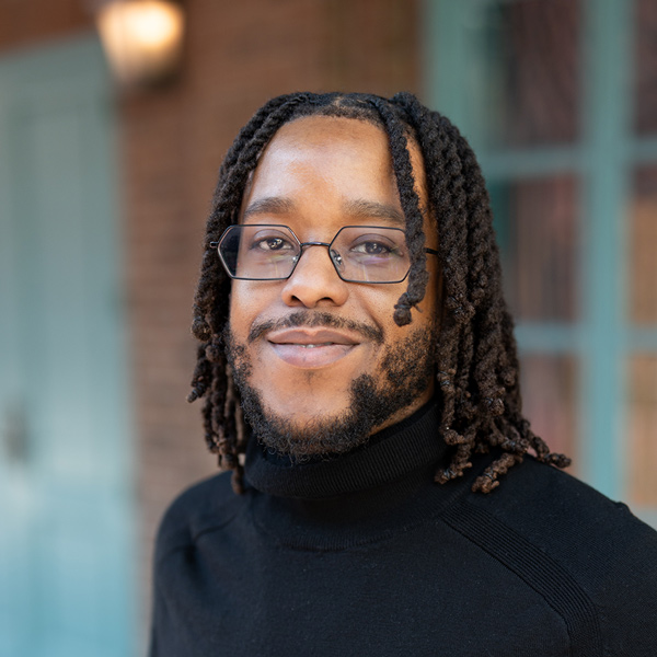 Ken Duff, Executive Director at Walden Place Senior Living, smiling in a professional headshot, wearing glasses and a black turtleneck, with a softly blurred outdoor background featuring brick and window details.