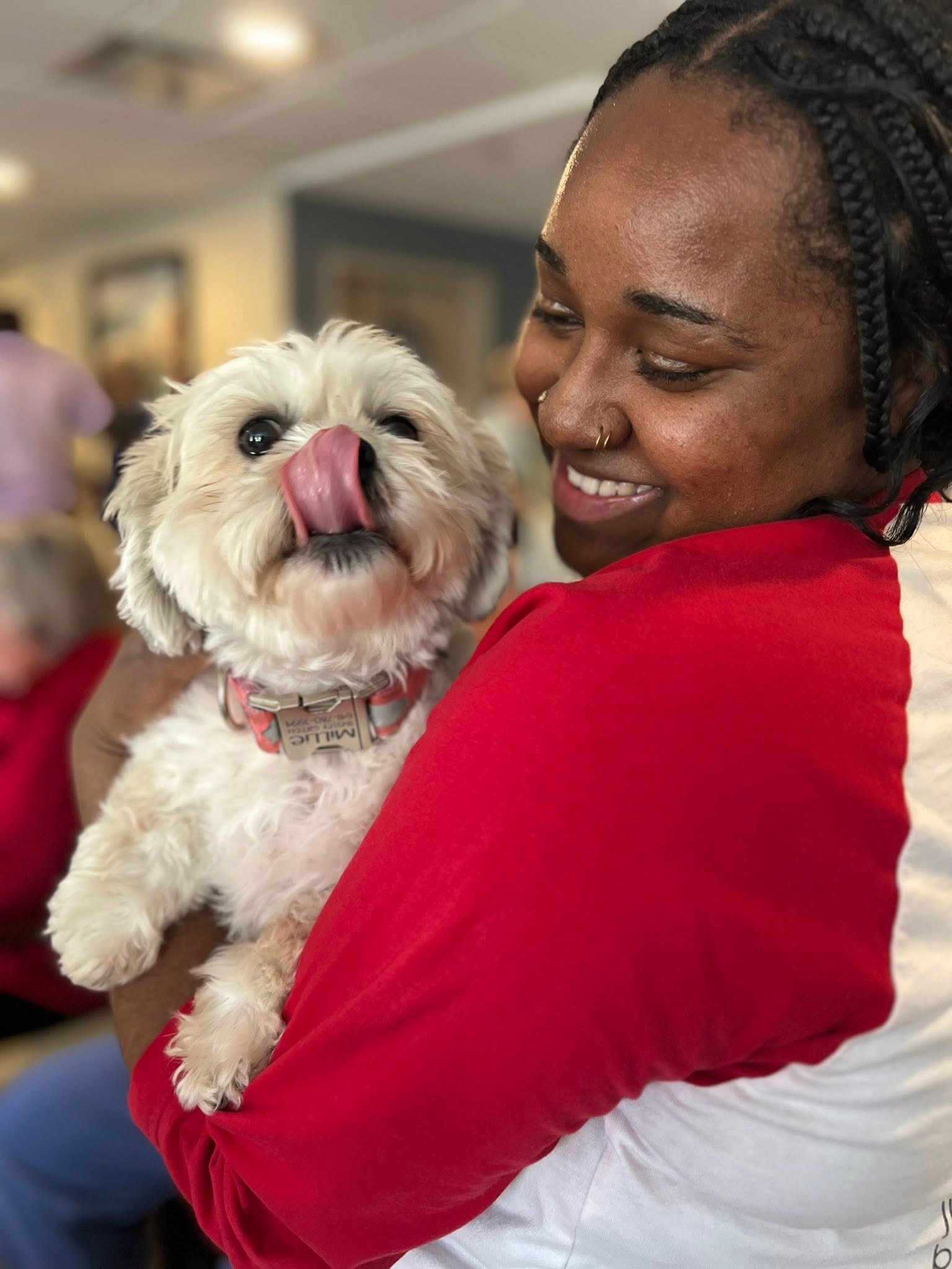 Team member smiles while holding a small white dog during a joyful pet-friendly moment in a senior living community.